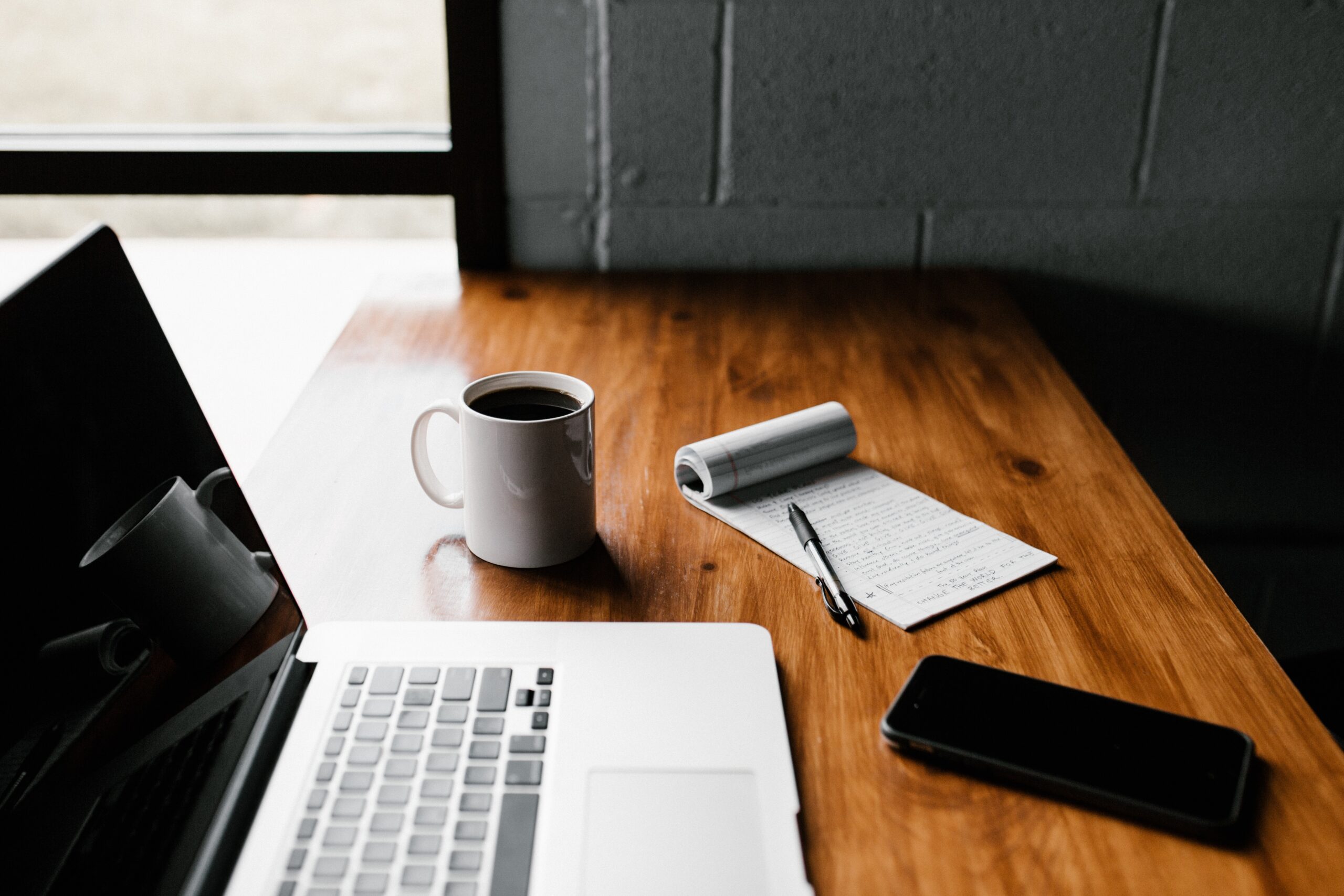 A clean desk with laptop, notepad and coffee.